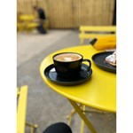 A cappuccino sit on a bright yellow metal table, outside.