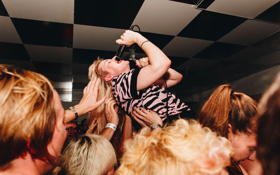 A singer is being lifted up by the crowd at a gig.