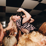 A singer is being lifted up by the crowd at a gig.