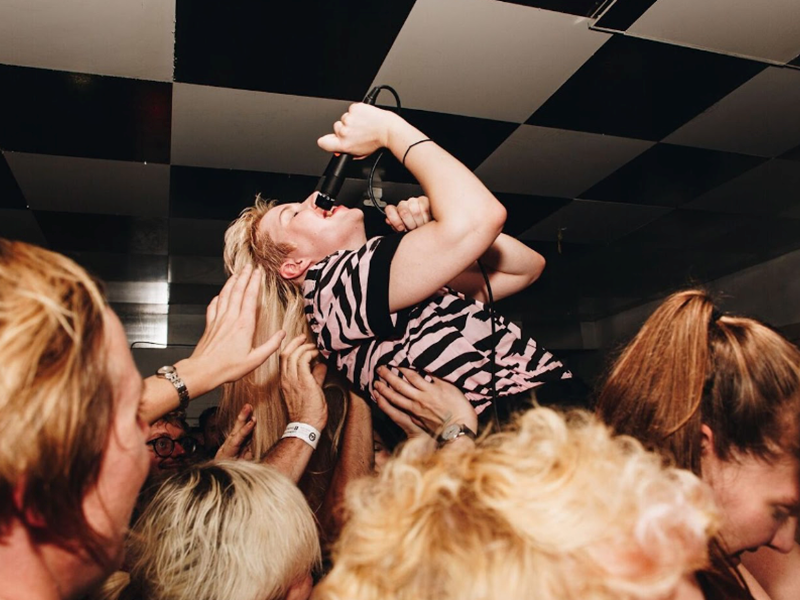 A singer is being lifted up by the crowd at a gig.