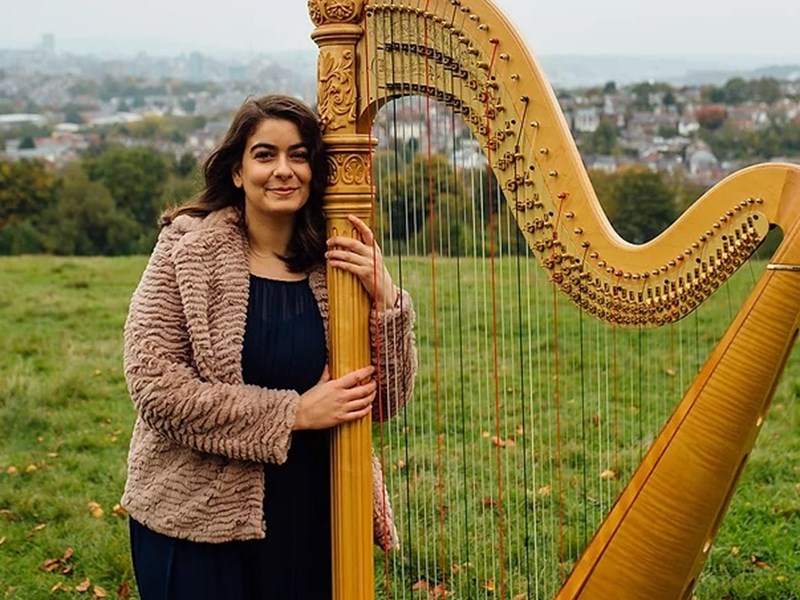 Imogen Garnettand her harp, in a field.
