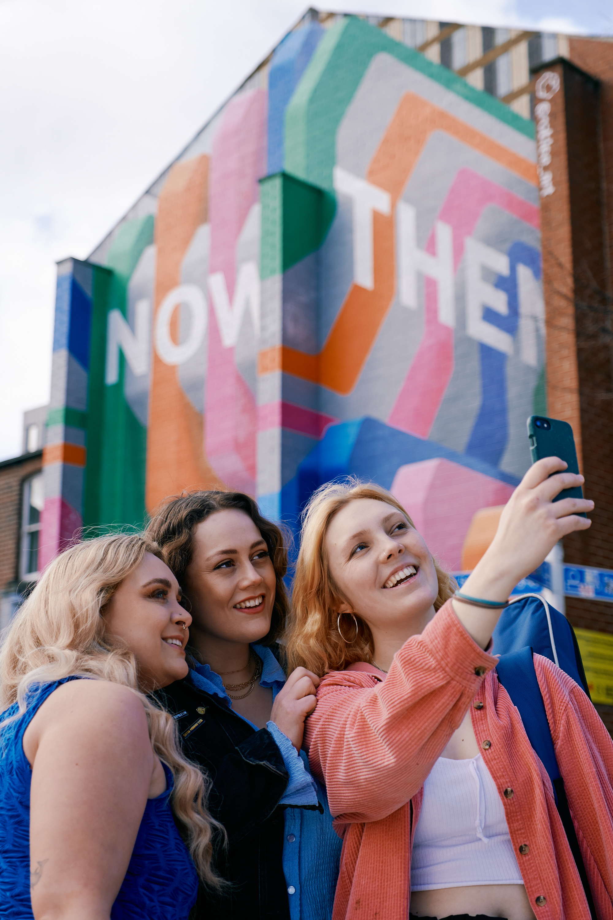 Three women take a selfie in front of the Now Then mural on Howard Street in Sheffield city centre.