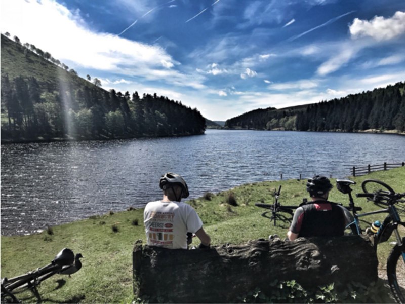 Two people sat by a lake, having a break while road cycling.