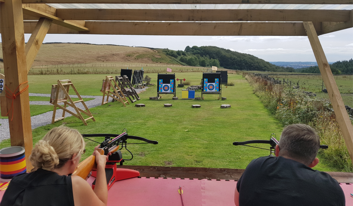 A man and a woman aiming crossbows at targets on a shooting range.