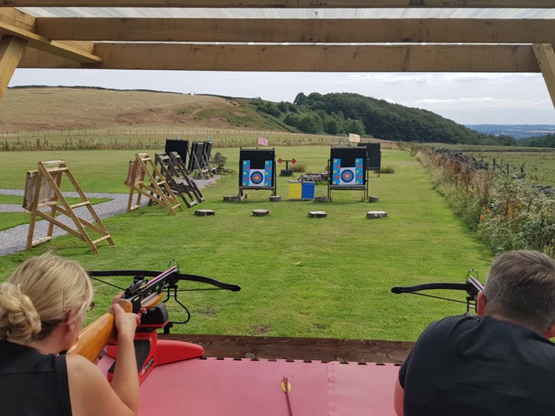 A man and a woman aiming crossbows at targets on a shooting range.