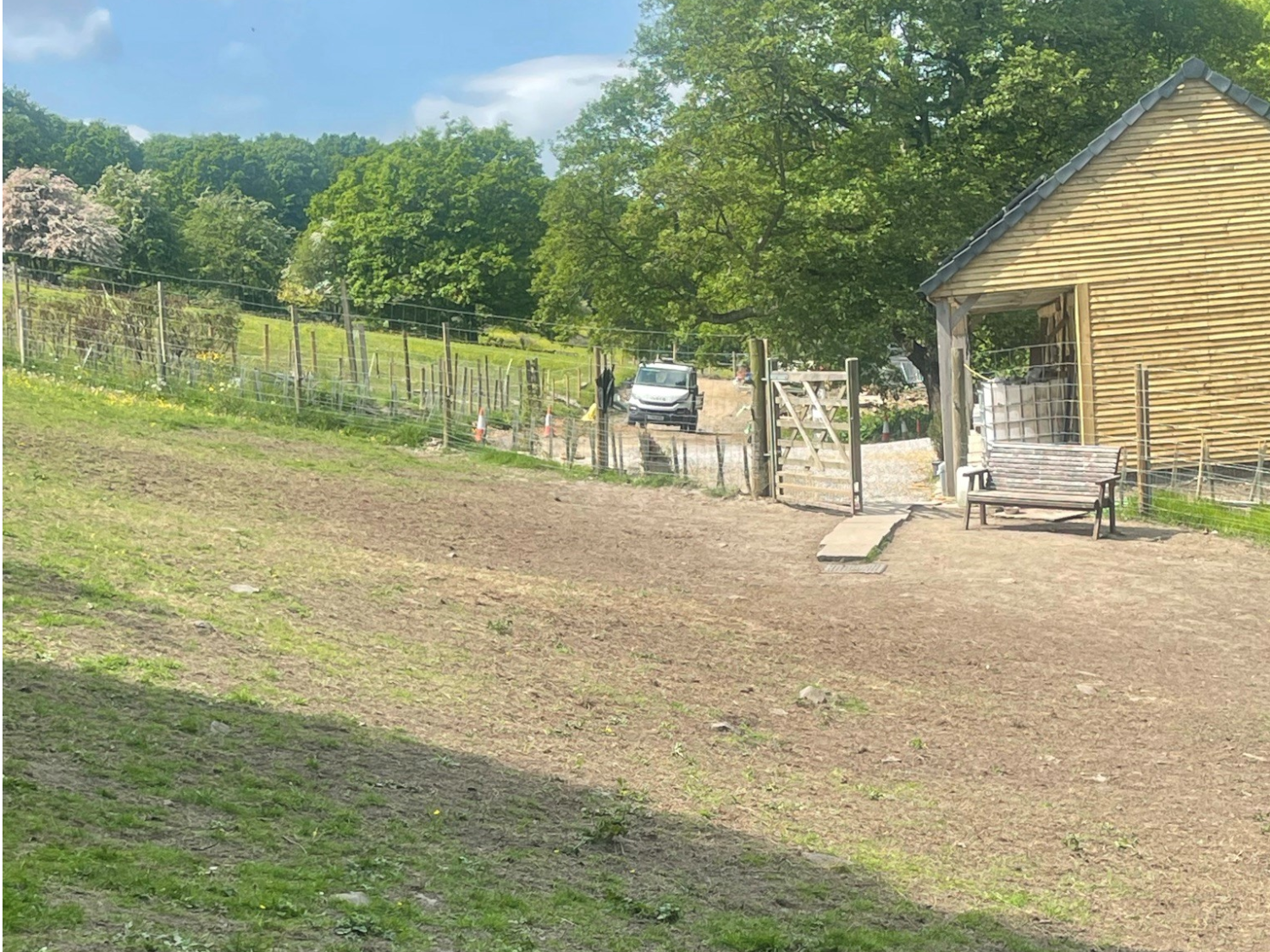 A fenced in grass area plus a bench and a wooden building at Rivelin Valley Dog Park.
