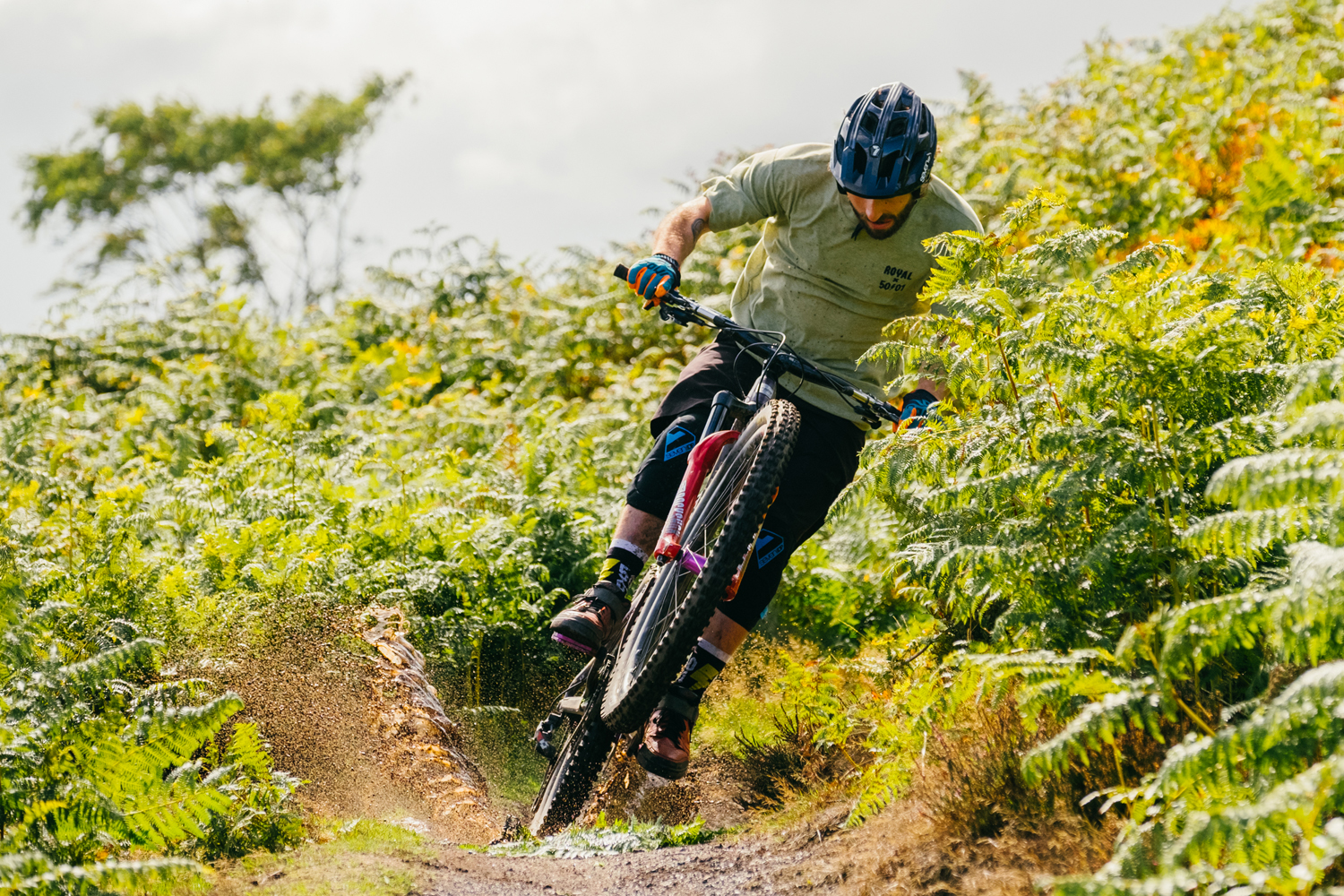 Male mountain biker riding through a dirt track in a leafy setting.
