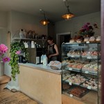 Insides Eve Kitchen. A person stands behind the counter. Inside a glass display case is a range of pastries and cakes.