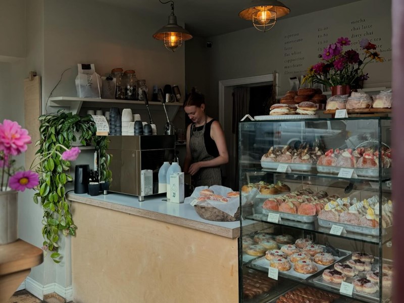 Insides Eve Kitchen. A person stands behind the counter. Inside a glass display case is a range of pastries and cakes.