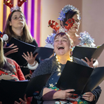 A choir, dressed in festive Christmas themed attire, performing.