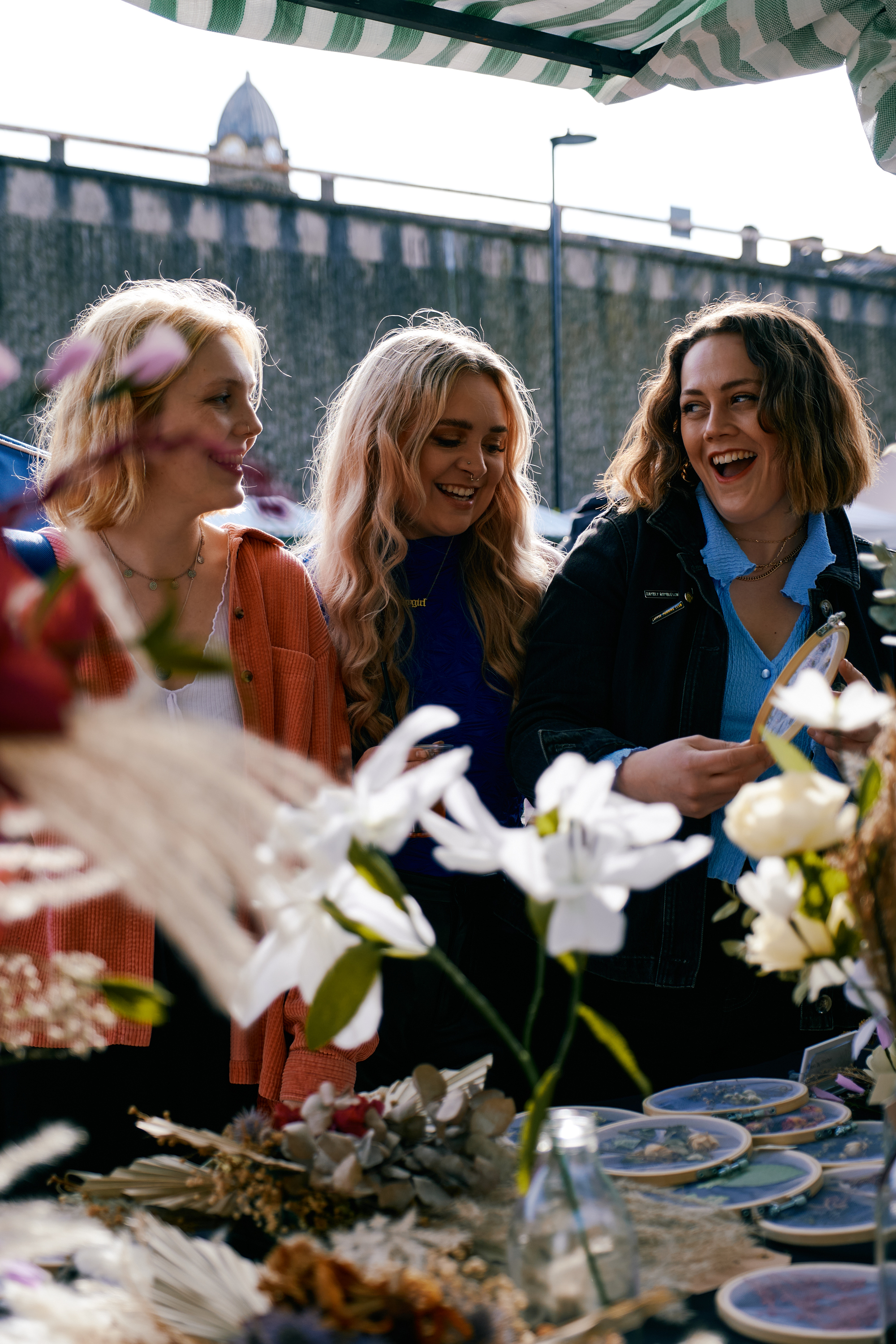 Three women looking through the goods on display on a stall at an outdoor market.