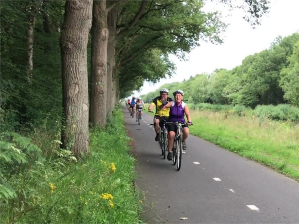 People cycling on a road through a wooded area.