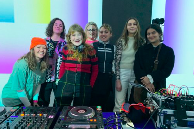 A group of people standing behind DJ decks.