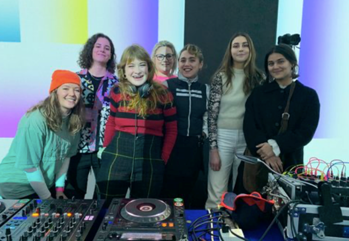 A group of people standing behind DJ decks.