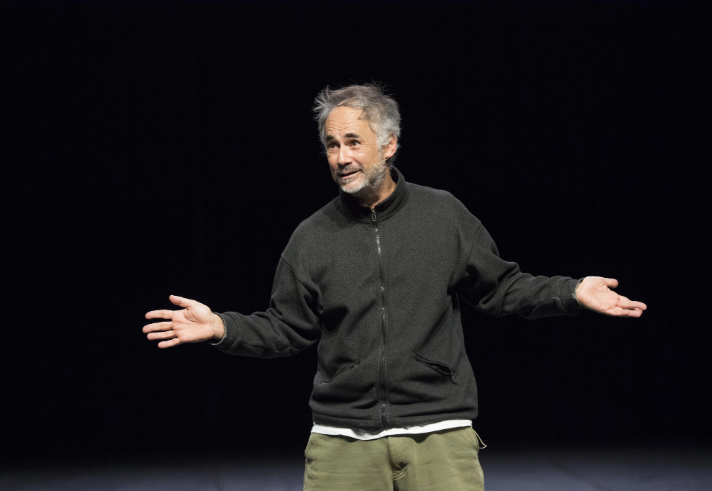 A man standing on a stage with his arms outstretched.
