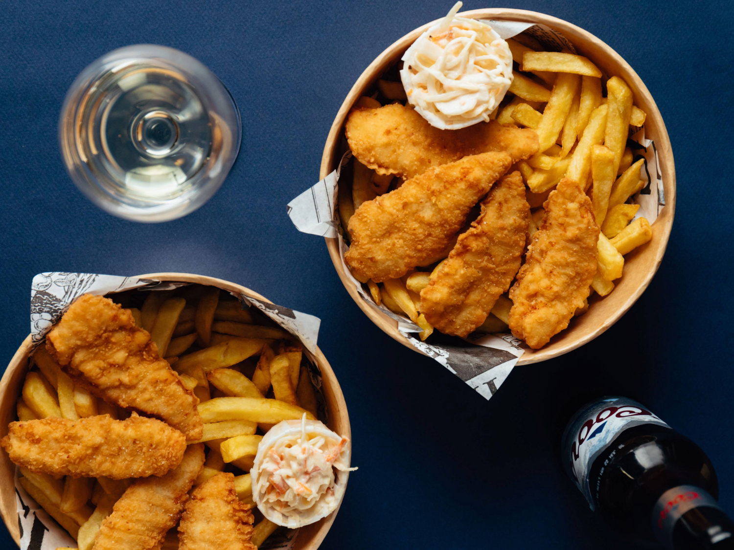 An overhead shot of two bowls of breaded chicken and chips and a bottle of beer.