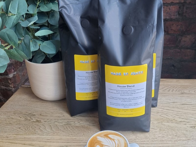 A cup of coffee on a table, along side some bags of coffee beans,  at Made by Jonty.
