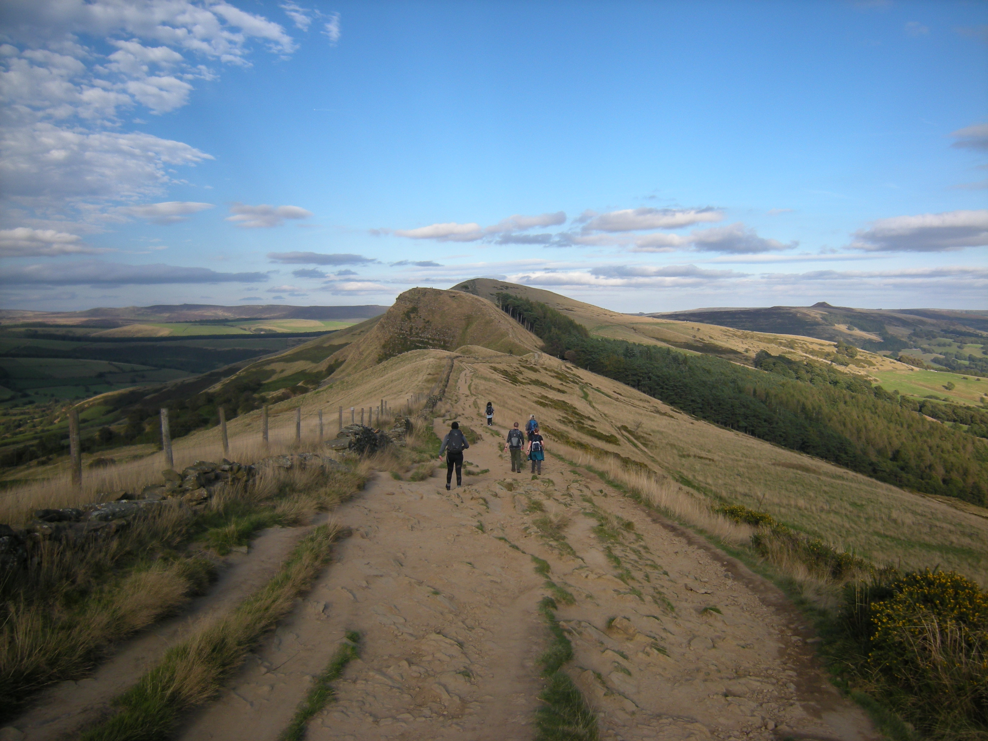 A rough track winding through hills in the countryside. In the distance you can see various groups of people out walking.