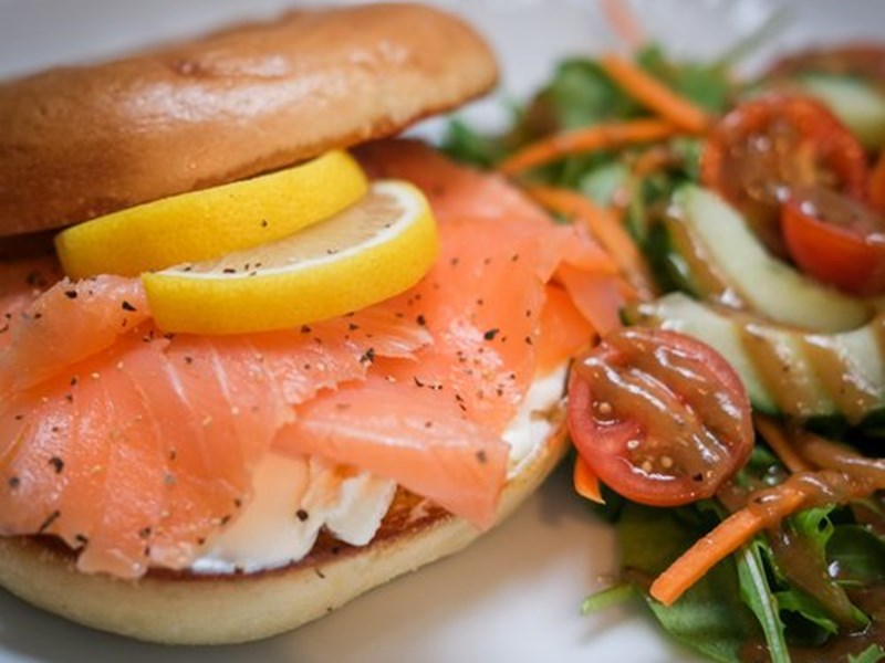 A bagel on a plate, filled with salmon and cream cheese and a side salad.