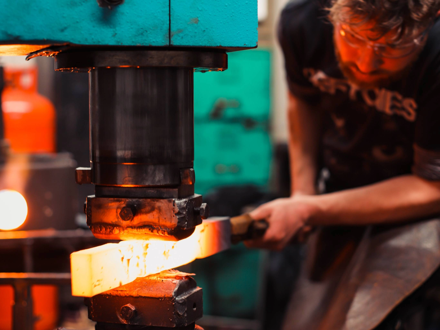 A man shaping a piece of white-hot metal in a huge press.