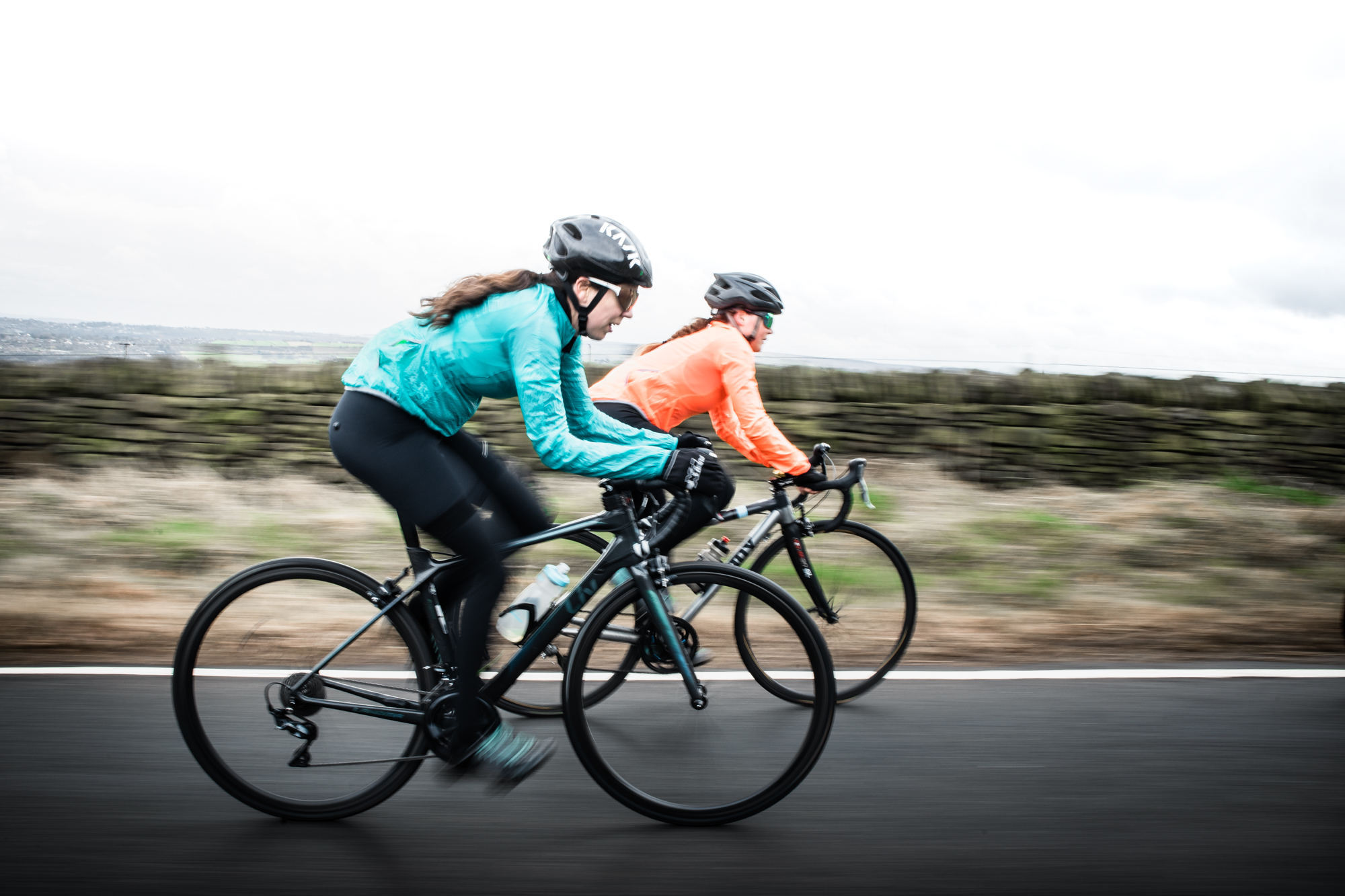 Two female cyclists riding their bikes in the countryside, the background is blurred as they speed past.
