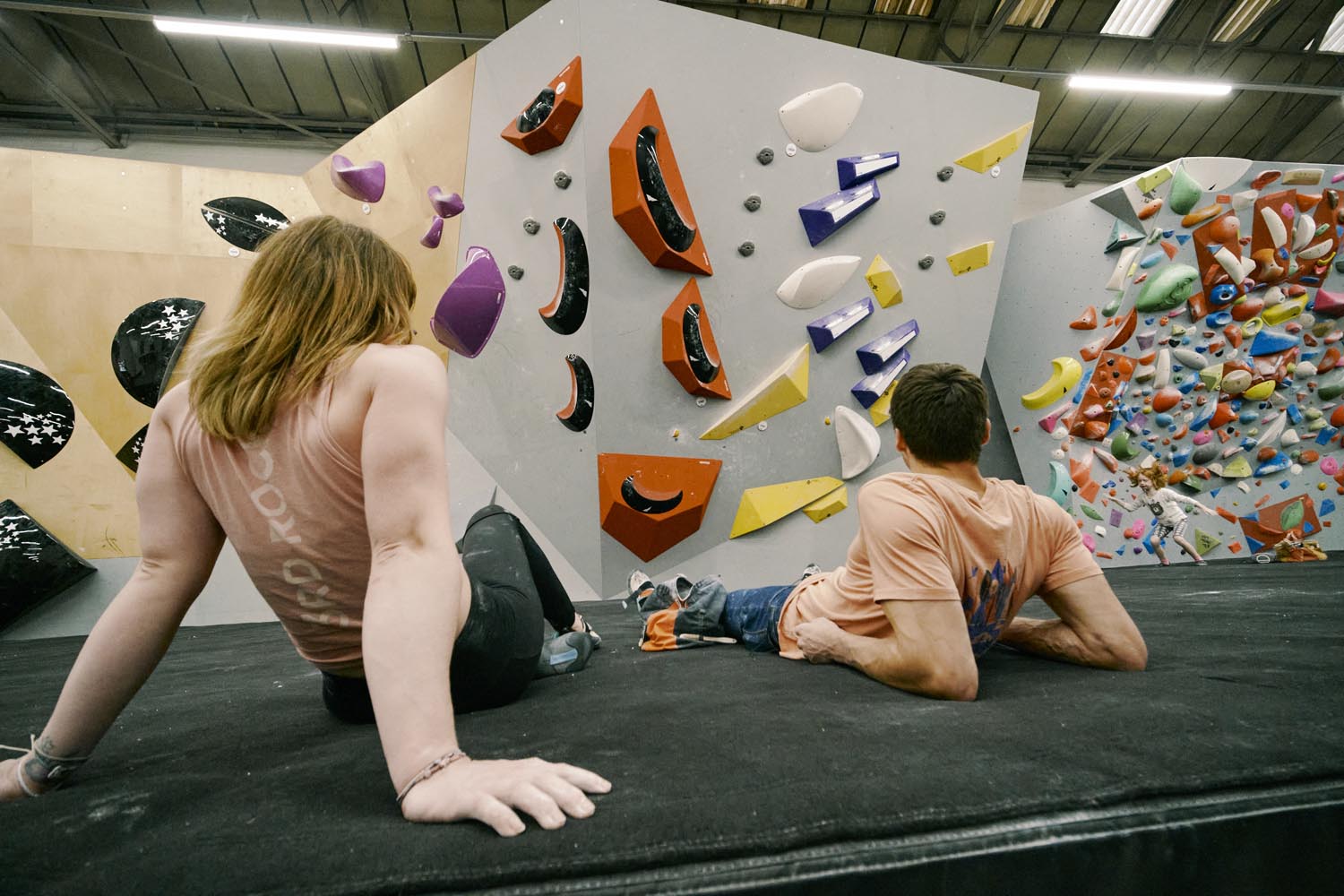 Two people are lying on the floor having a rest at an indoor climbing centre.