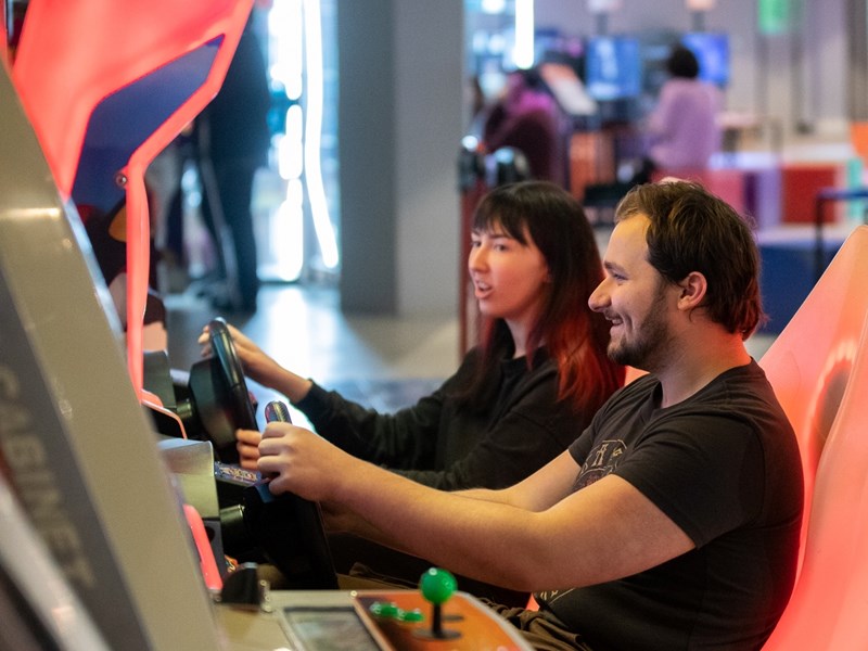 Two people playing a driving game The National Videogame Museum.