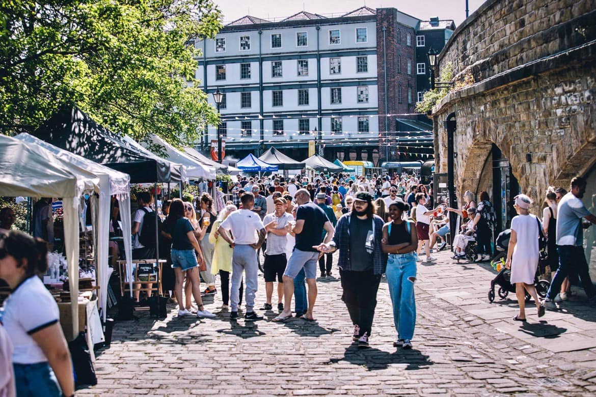 Sunny day as people walk along the cobbled quayside 