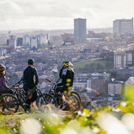 Five people are sat on mountain bikes on hill overlooking Sheffield city centre.