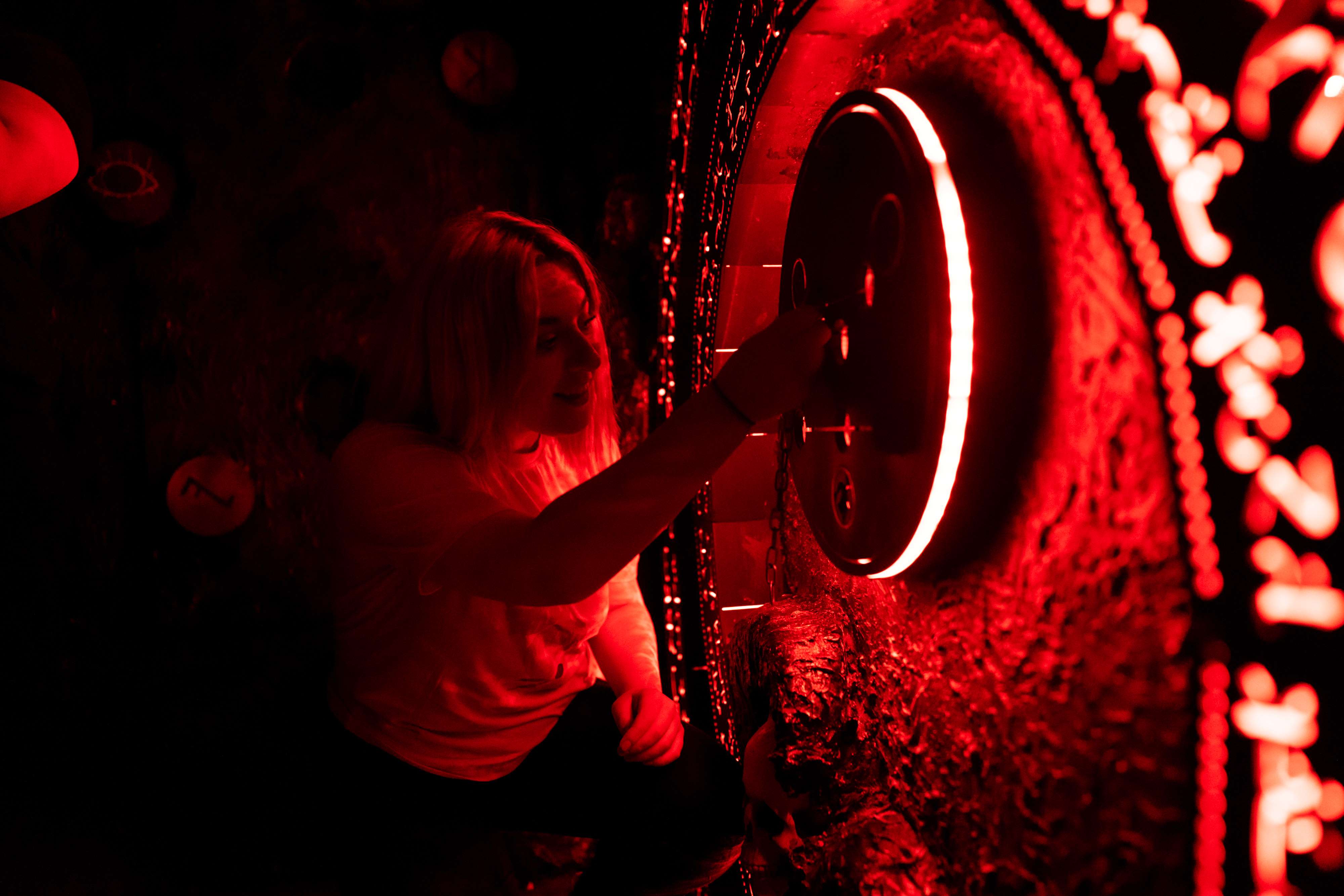 A woman trying to solve a puzzle in a dimly lit room at The Great Escape Game.