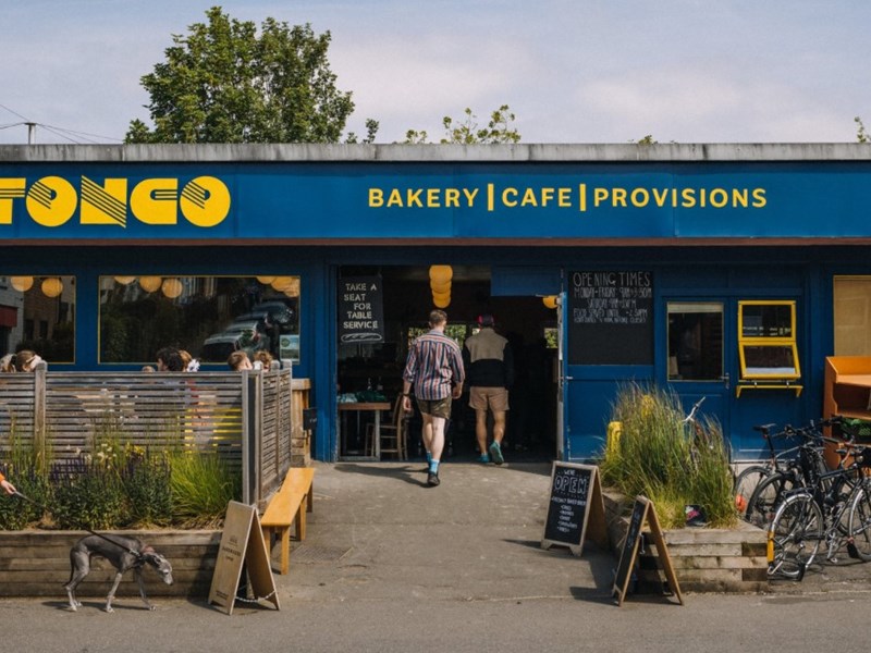The exterior of a building painted blue. There is yellow lettering above the window and door that reads ' Tonco' and 'Bakery, Cafe, Provisions'.