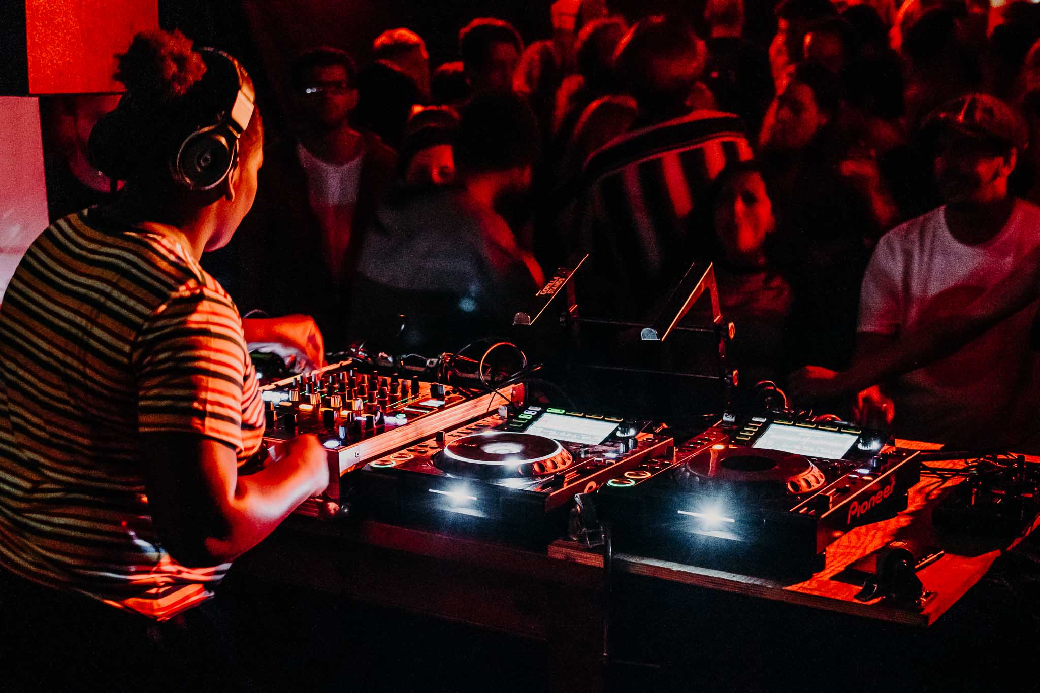 A female DJ of African heritage is mixing at the decks, for a nightclub crowd.