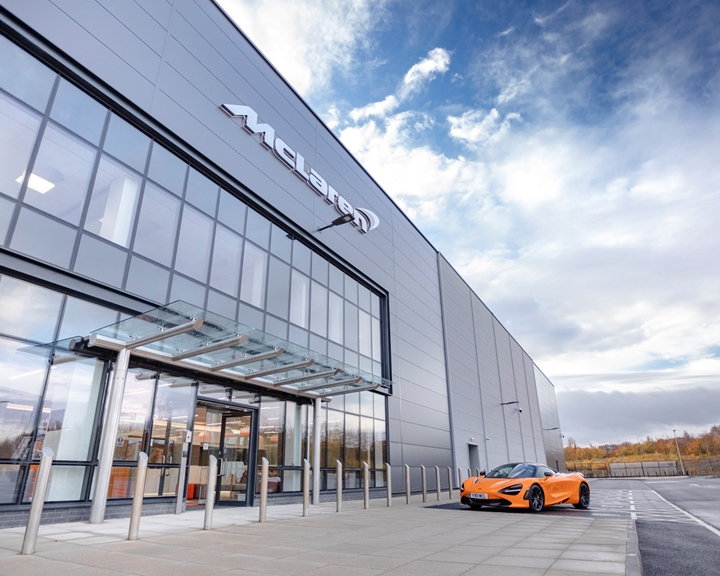 An orange McLaren car parked outside the glass McLaren building at The Advanced Manufacturing Innovation District.