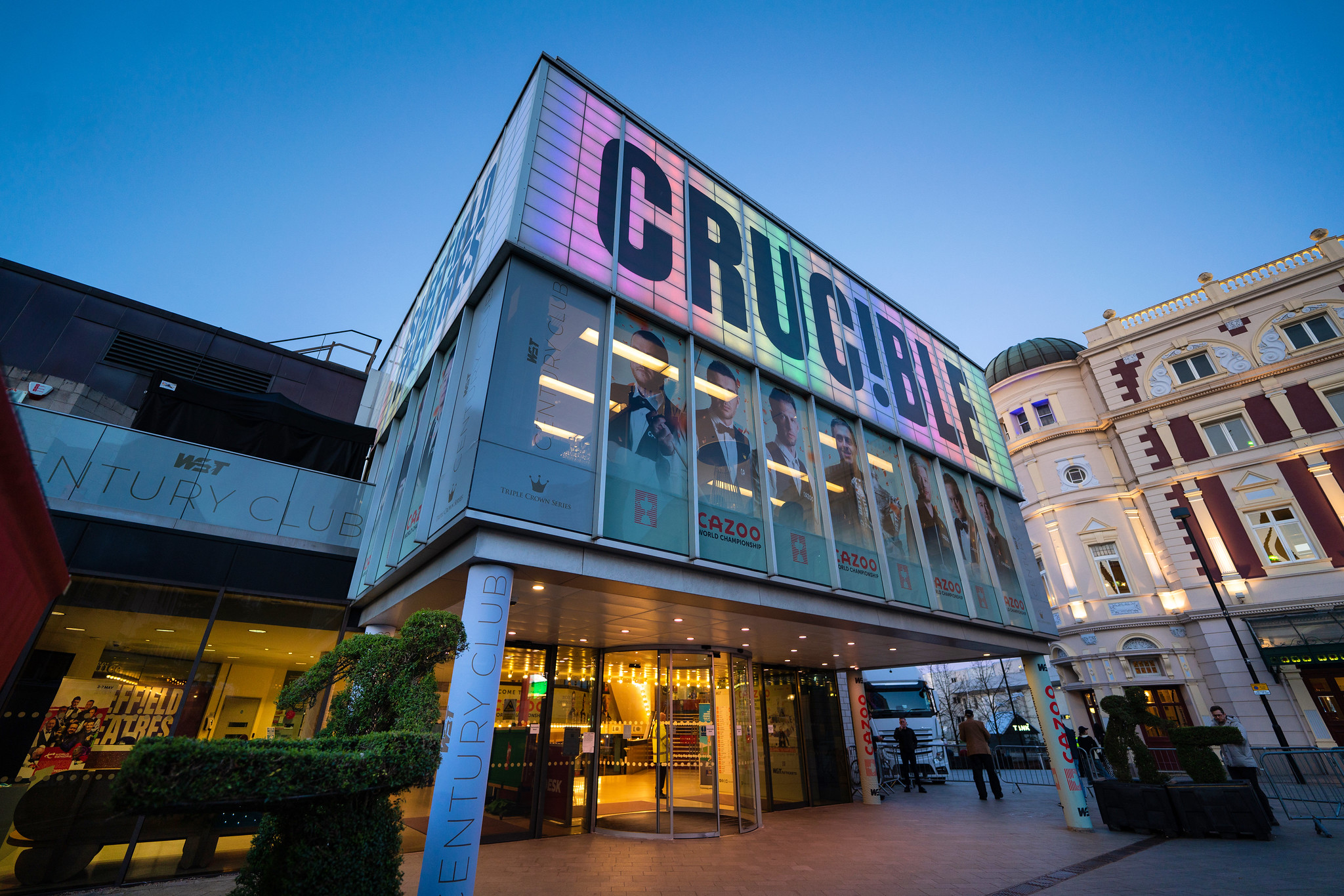 The exterior of the Crucible Theatre, lit up in the dusk with colourful light.