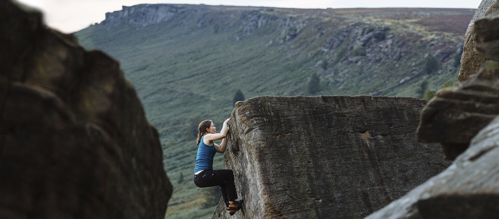 A woman climbing a rocky outcrop has nearly reached the top.