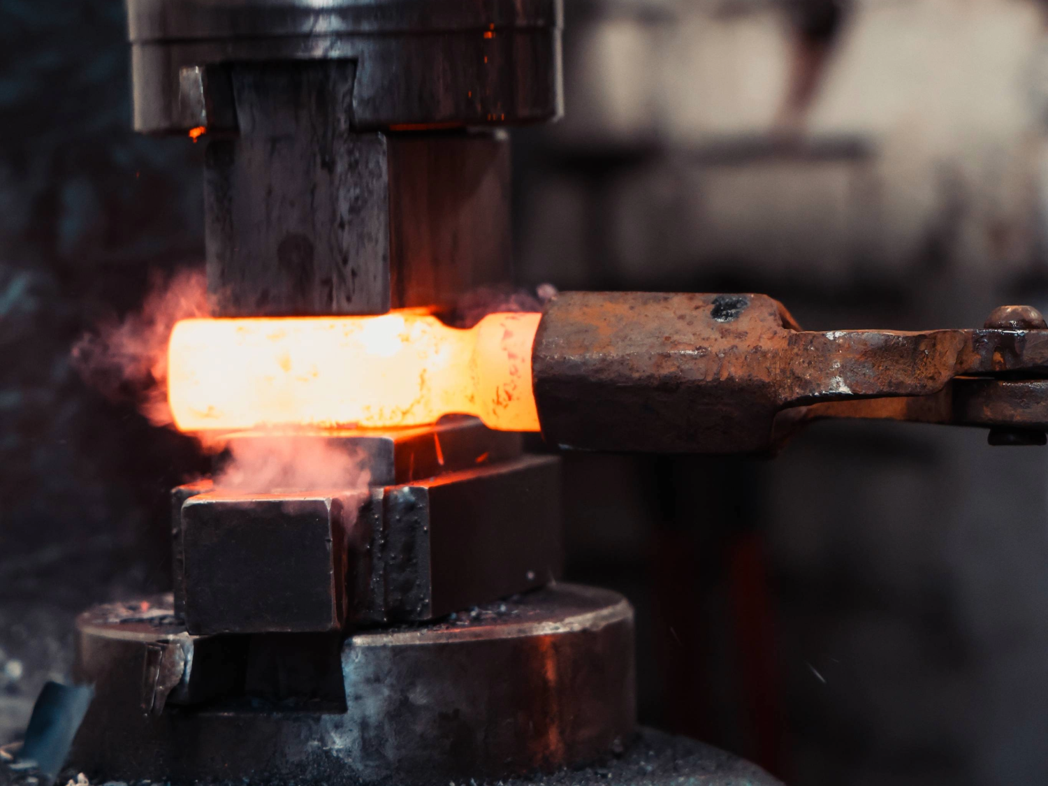 A piece of white-hot metal being shaped in a huge hammer press.