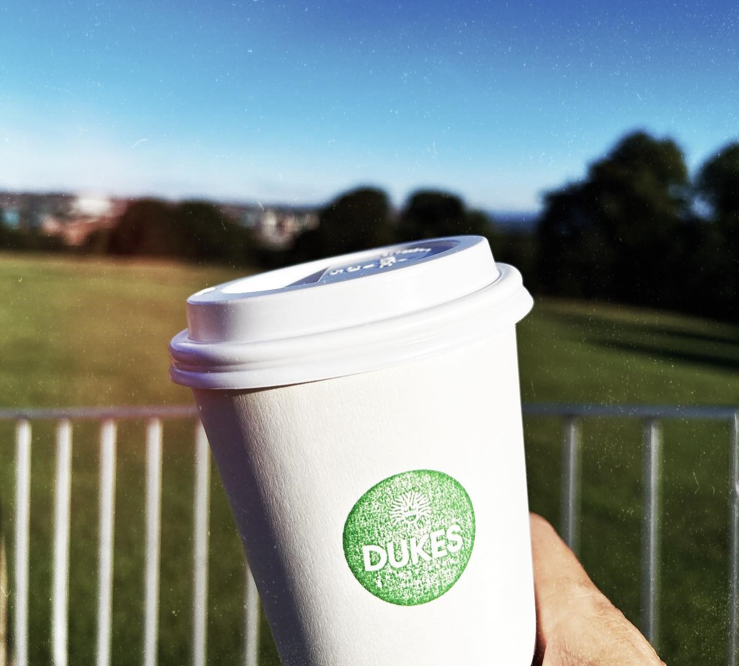 Dukes in the Park branded paper cup with the park in the background 