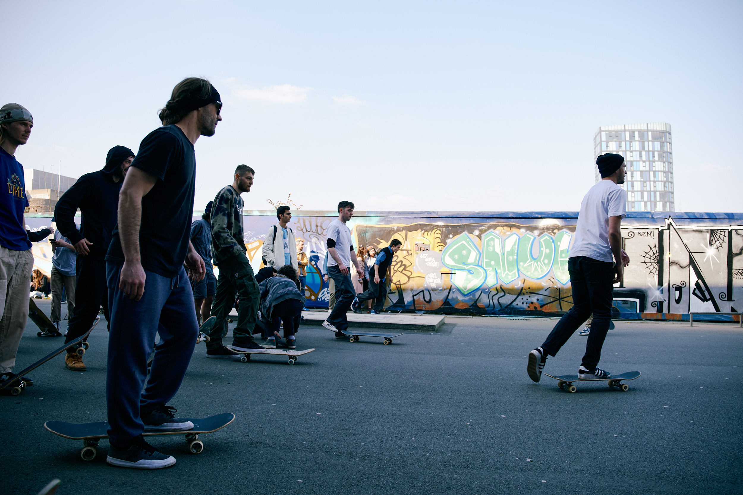 A dozen or so people are skateboarding in a small urban skate park.