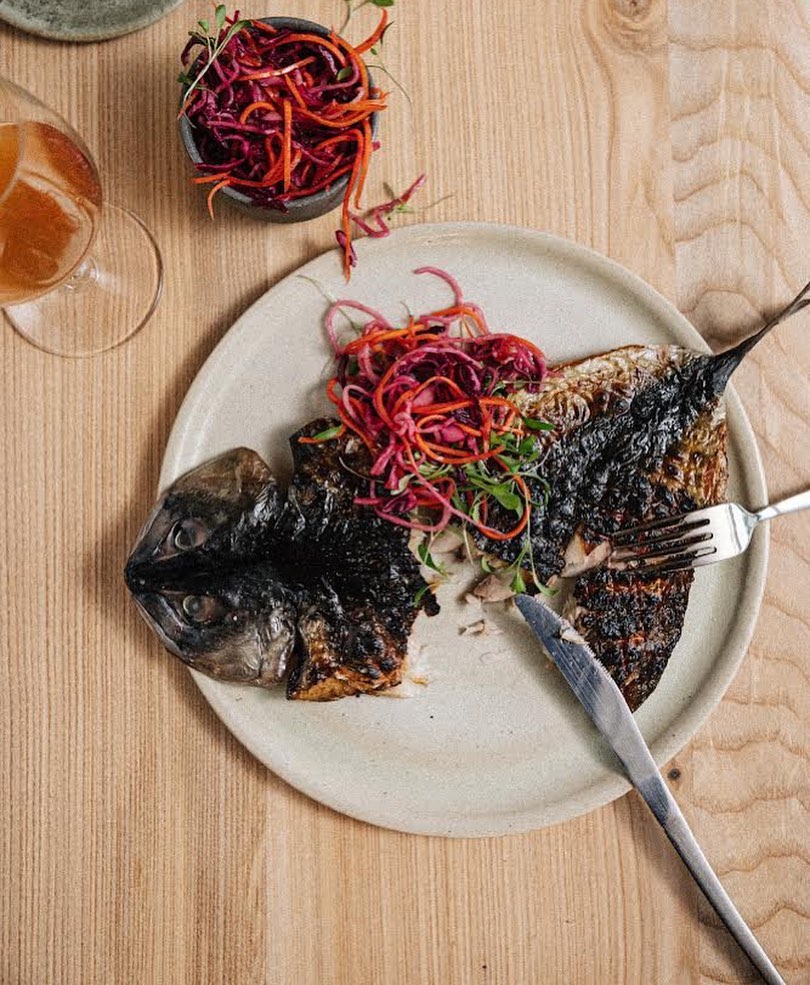 A plate with grilled fish set on a wooden table.