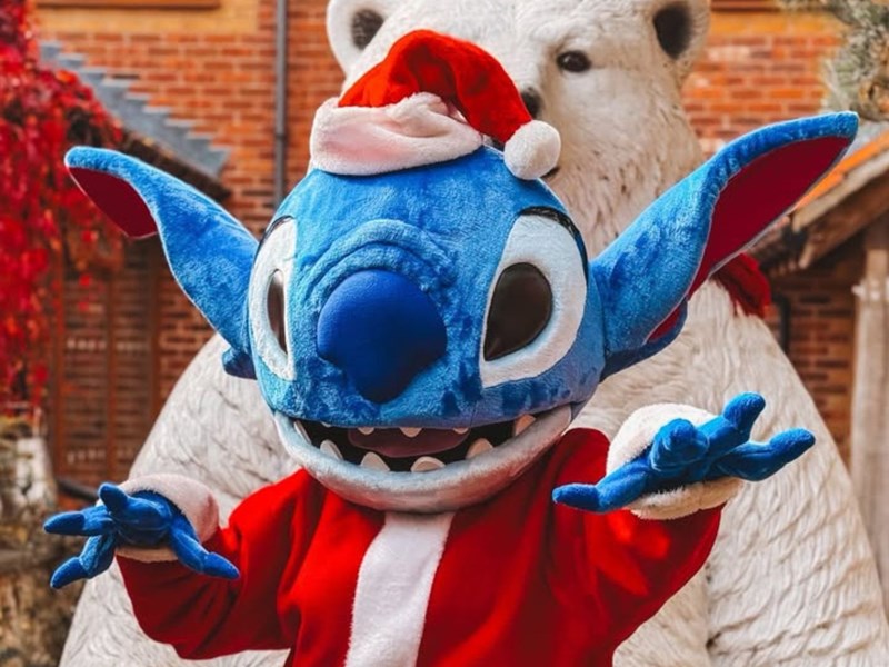 A person in a Stich costume, wearing a Santa outfit stands in front of a polar bear.