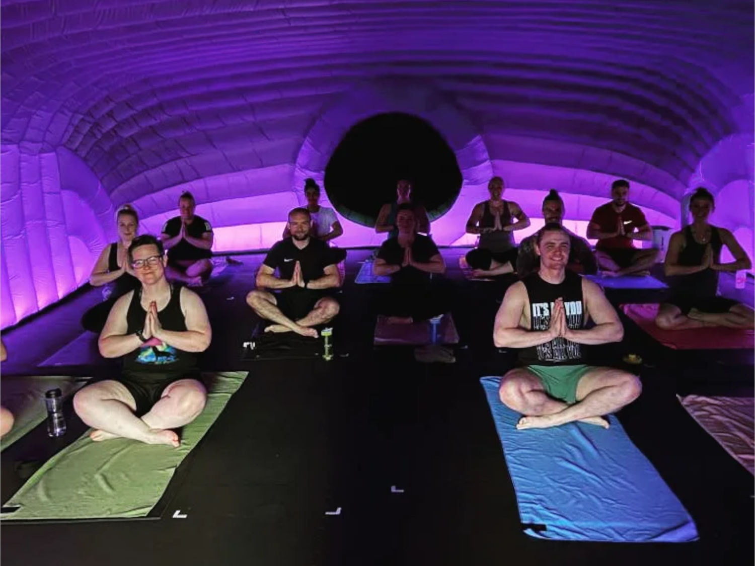 Twelve people are sat on mats on the floor doing yoga.