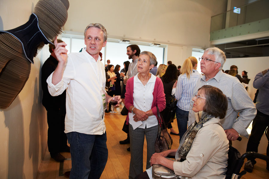 A busy and crowded room full of people looking at artworks that are displayed on the walls.