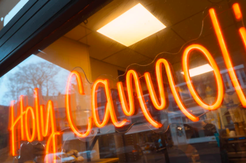An orange neon sign that reads 'Holy Cannoli'.