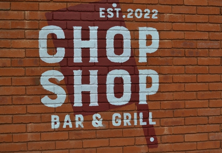 The Chop Shop Bar & Grill logo painted on a red brick wall.